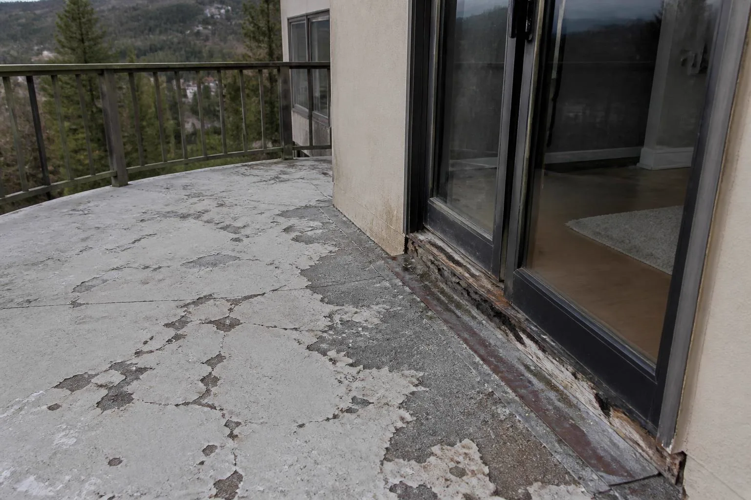 Failing exterior deck with cracked peeling waterproof coating and dry rot at the sliding door threshold on a foothill home near Auburn California